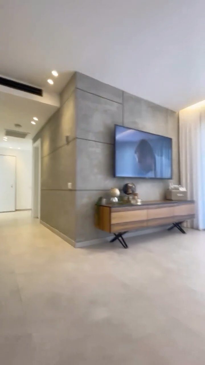 A television mounted on a grey concrete textured accent wall above a wooden sideboard.