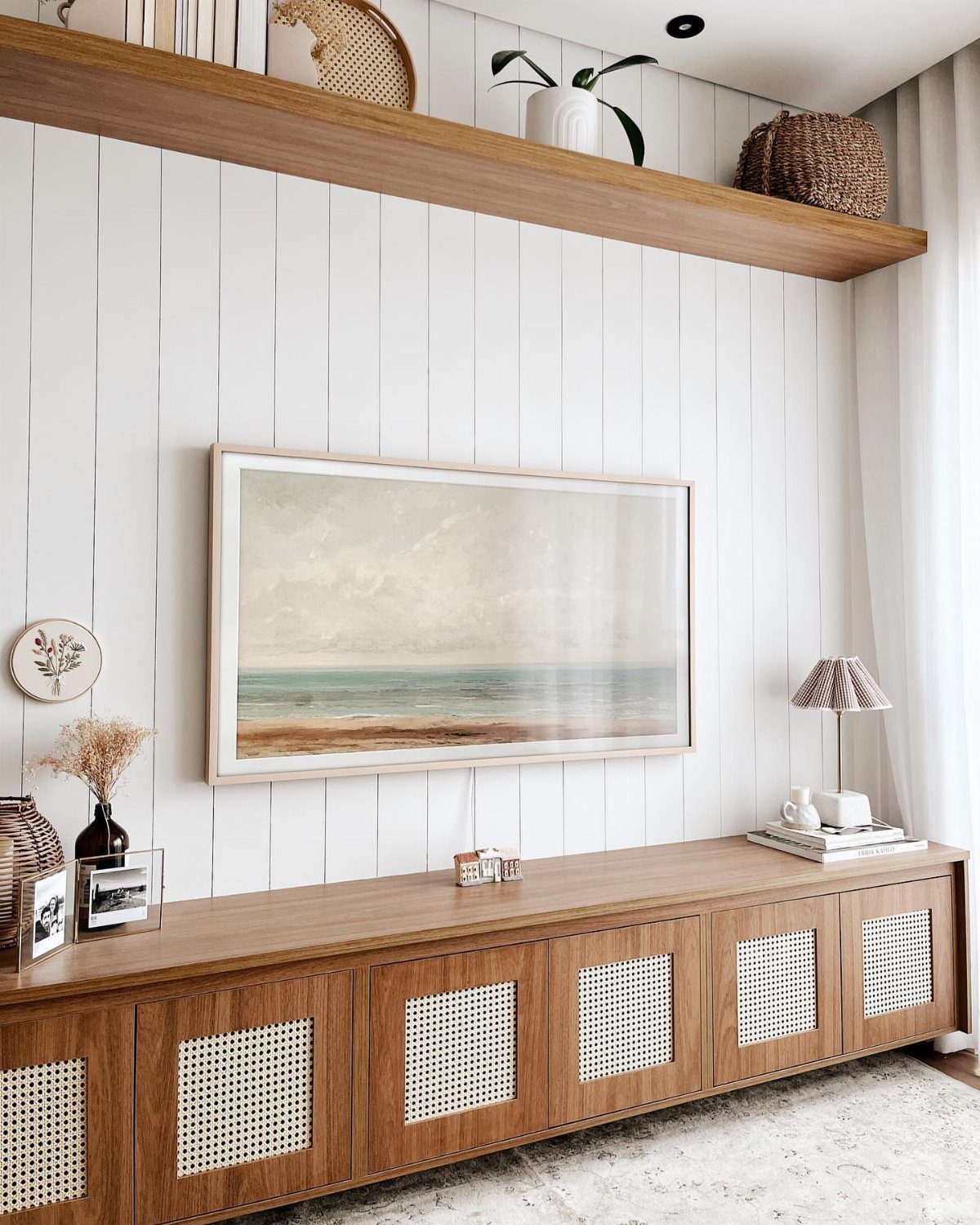 White vertical shiplap wall with a large framed landscape painting and wooden sideboard below.