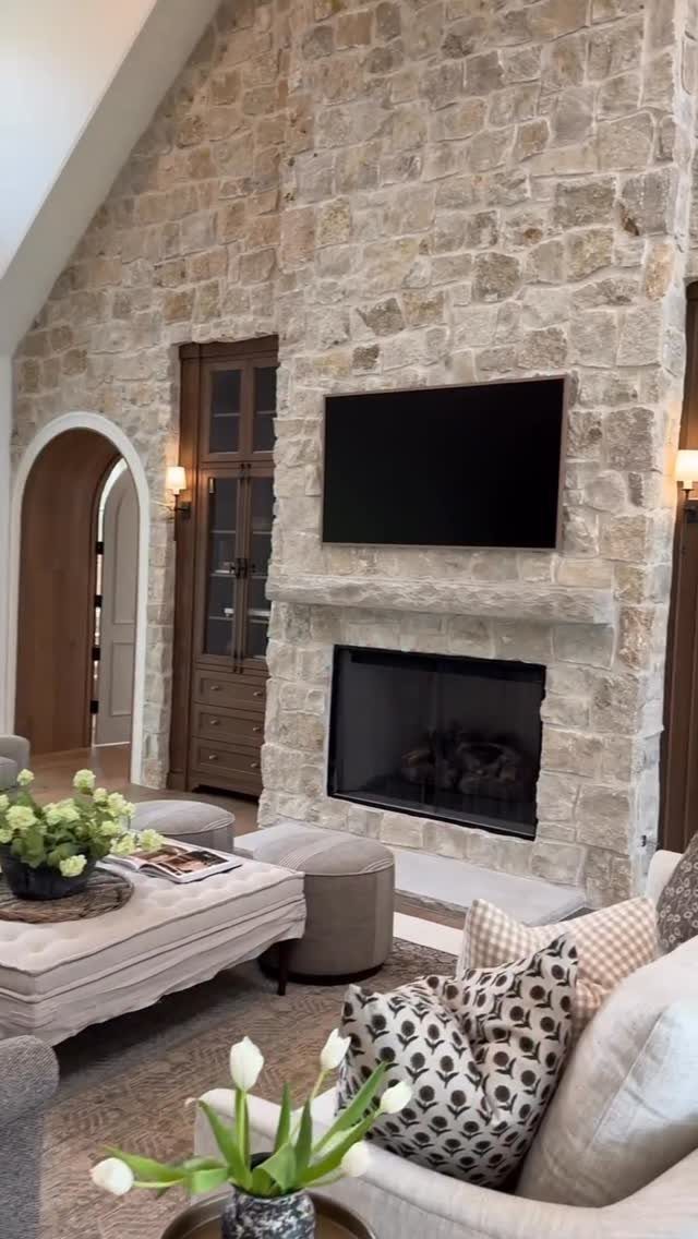 A large stone accent wall with a mounted television and fireplace in a living room.