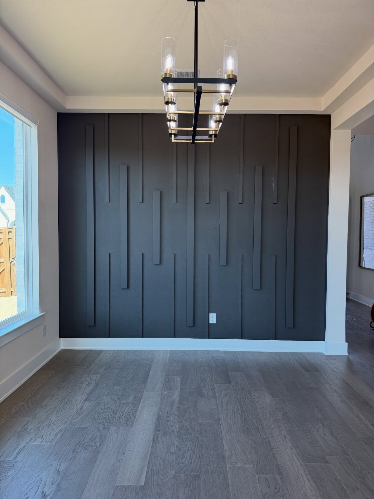 Dark grey accent wall with vertical wood trim pieces of varying lengths in a modern room.