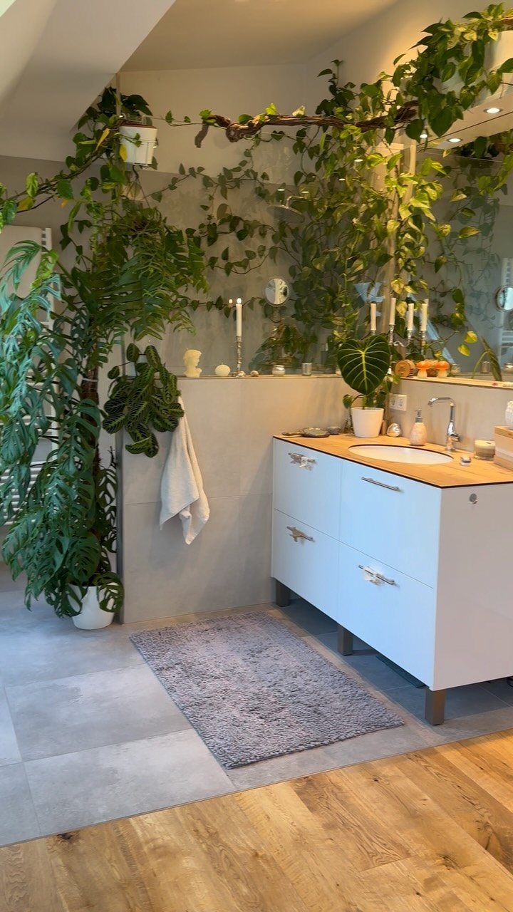 Green climbing plants and potted greenery decorating a modern bathroom wall above a white vanity.