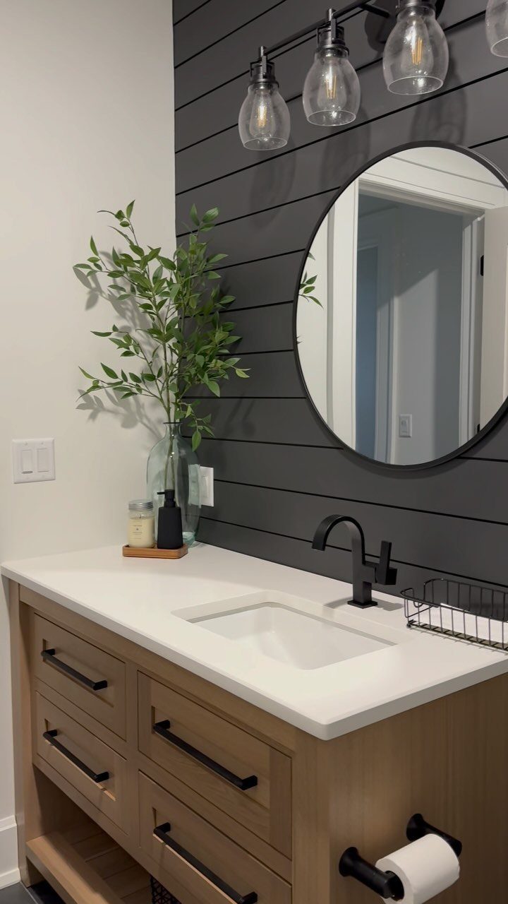 Dark gray shiplap accent wall behind a white bathroom vanity with a round mirror.
