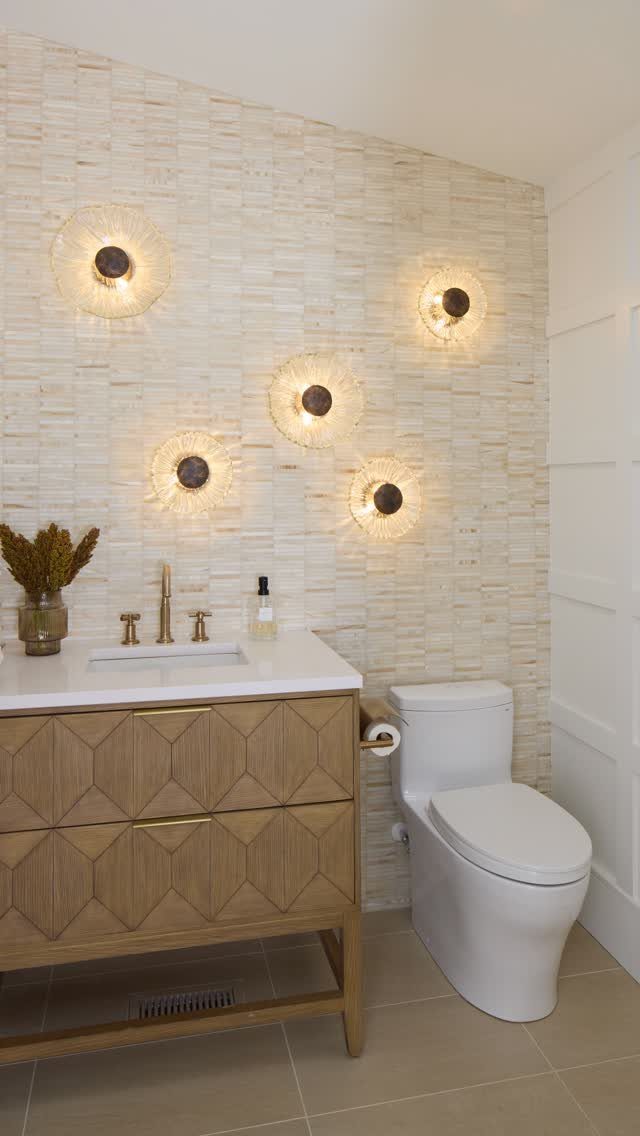 Textured mosaic tile wall with glowing circular sconces above a wooden vanity and white toilet.