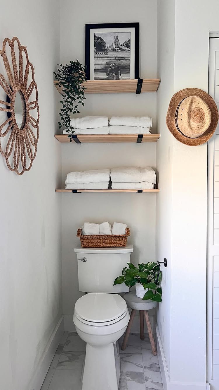 Wooden floating shelves holding white towels and a framed picture above a white toilet.