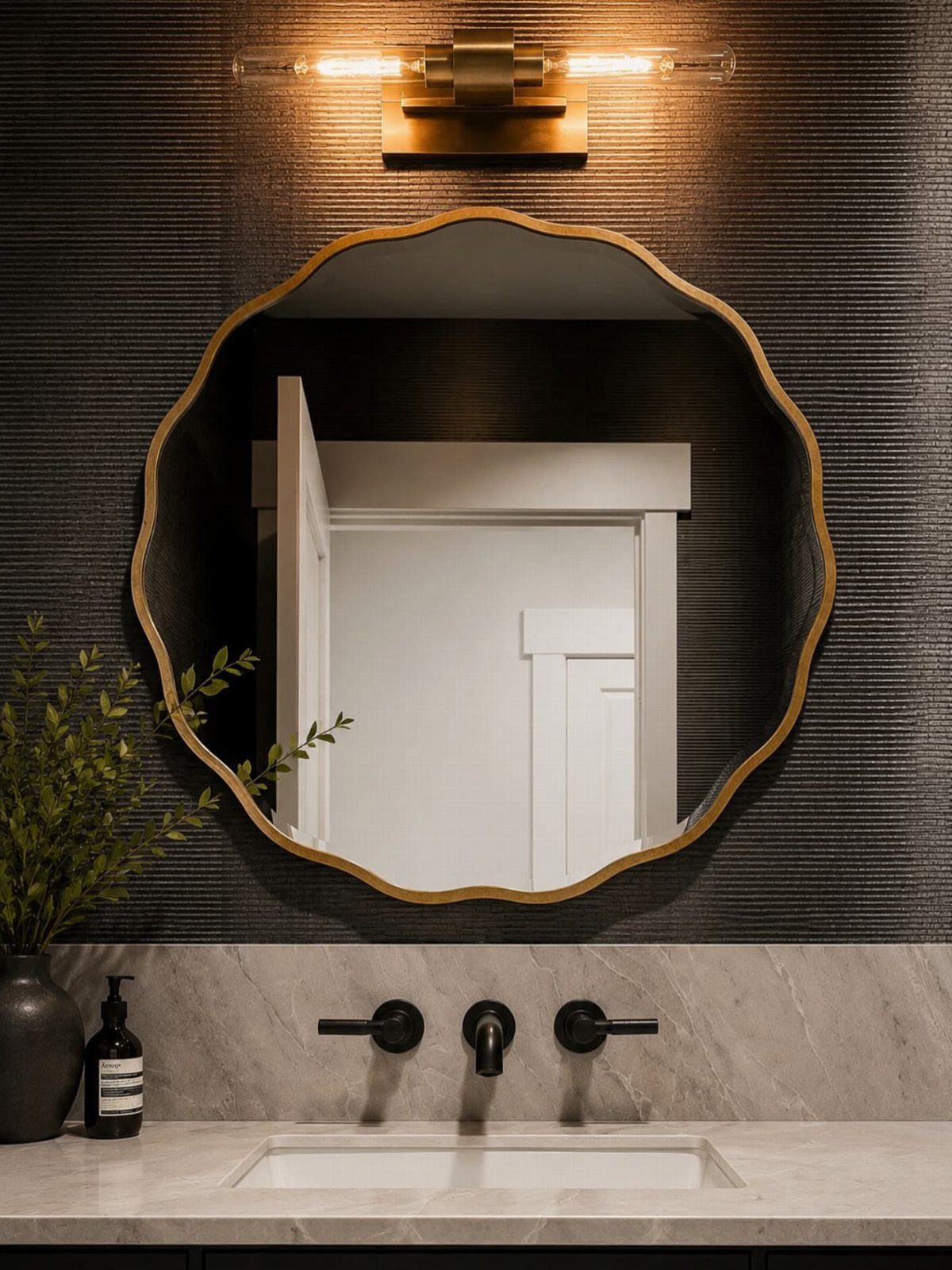 A gold scalloped mirror mounted on a dark textured wall above a marble vanity.