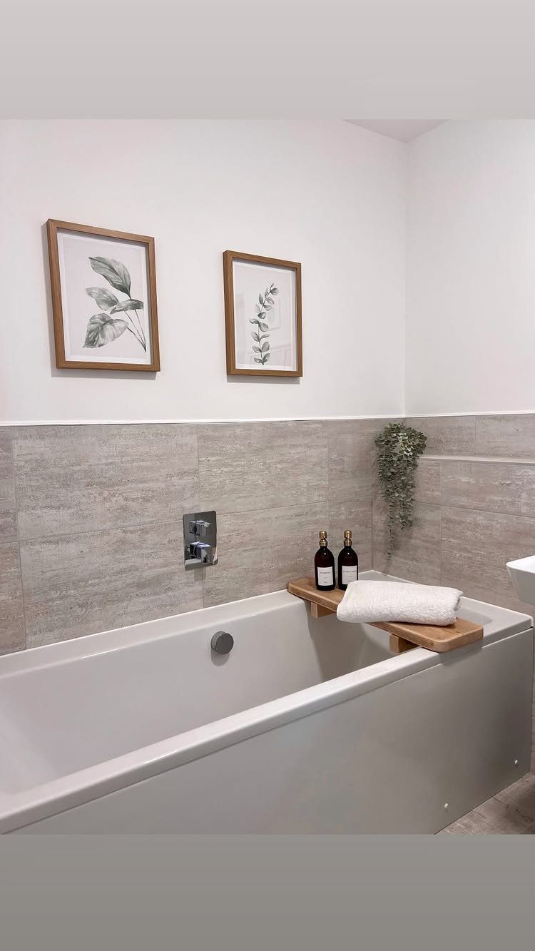 Two framed botanical art prints hanging on a white bathroom wall above a bathtub.