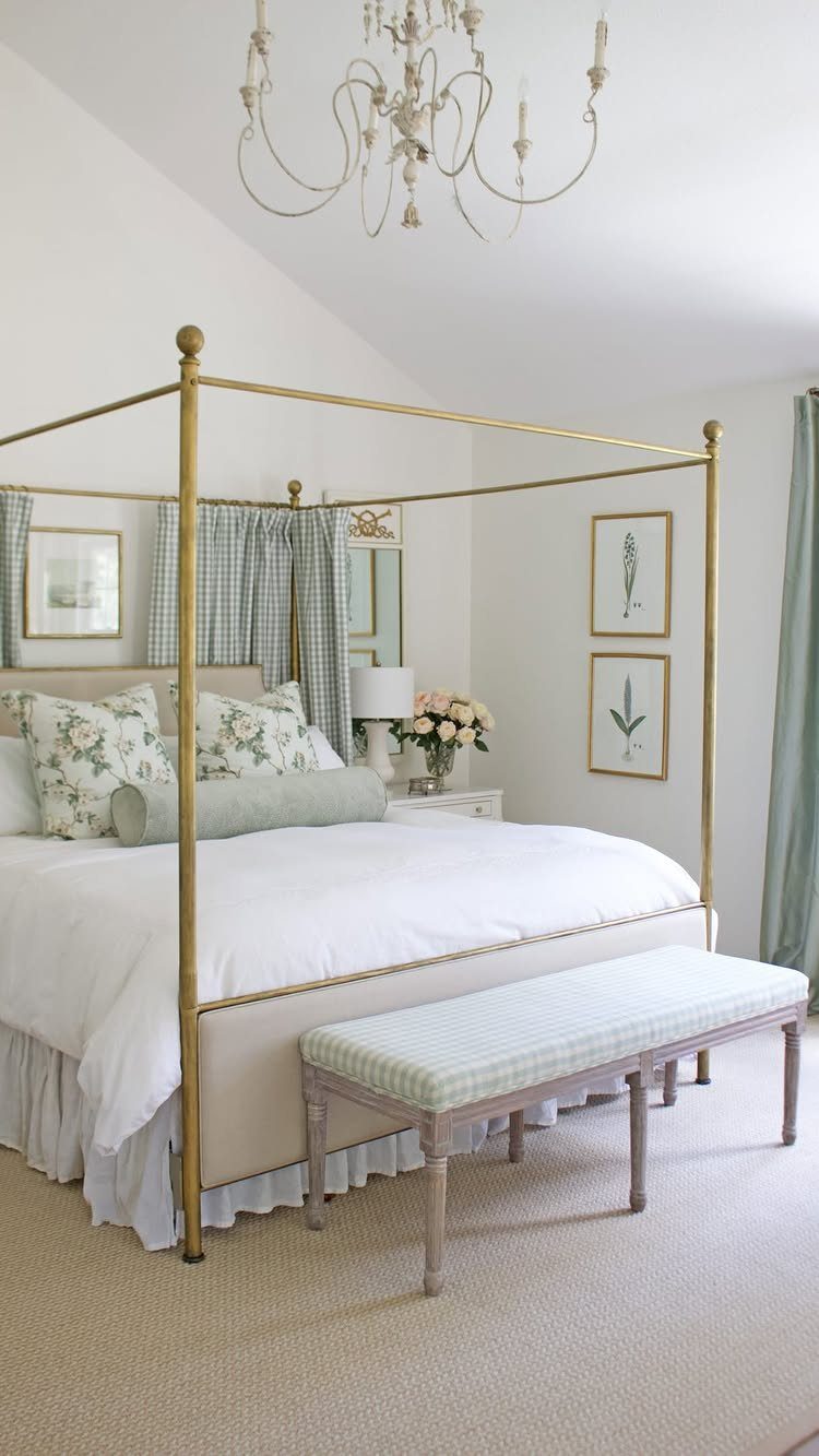A gold metal canopy bed with white linens and floral pillows in a bright bedroom.