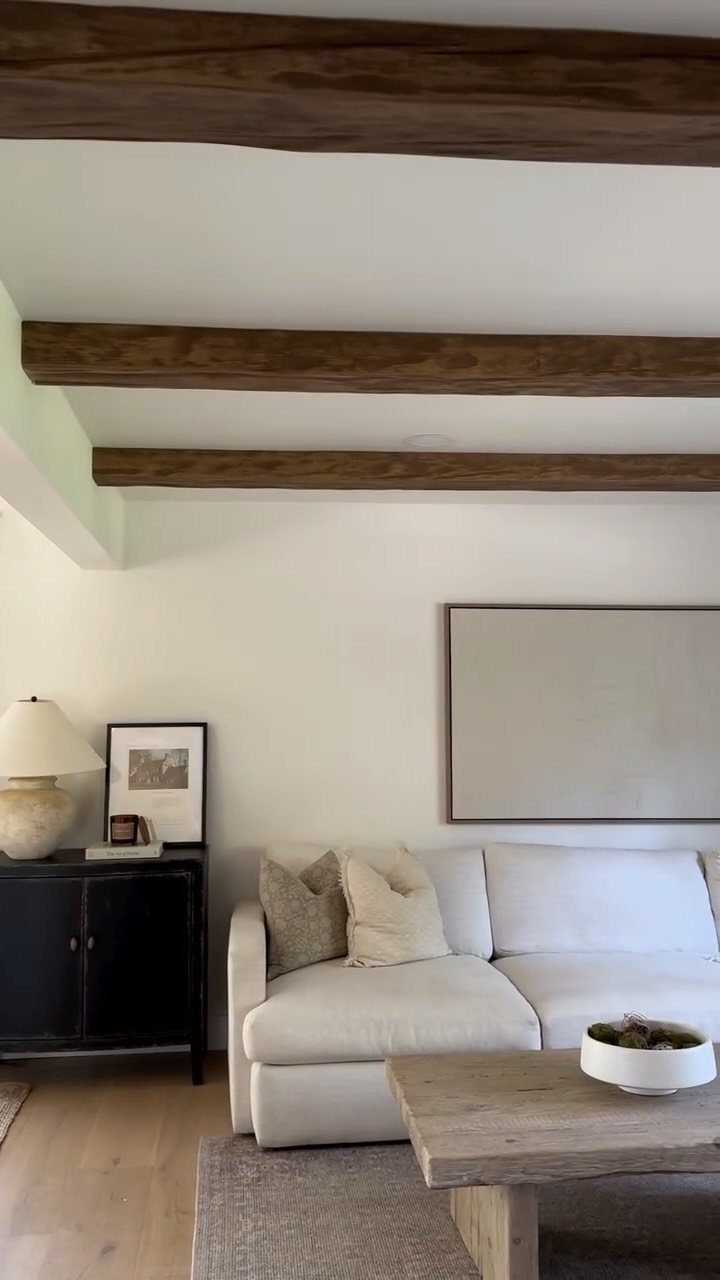 Dark wooden beams span across a white ceiling above a modern white living room sofa.