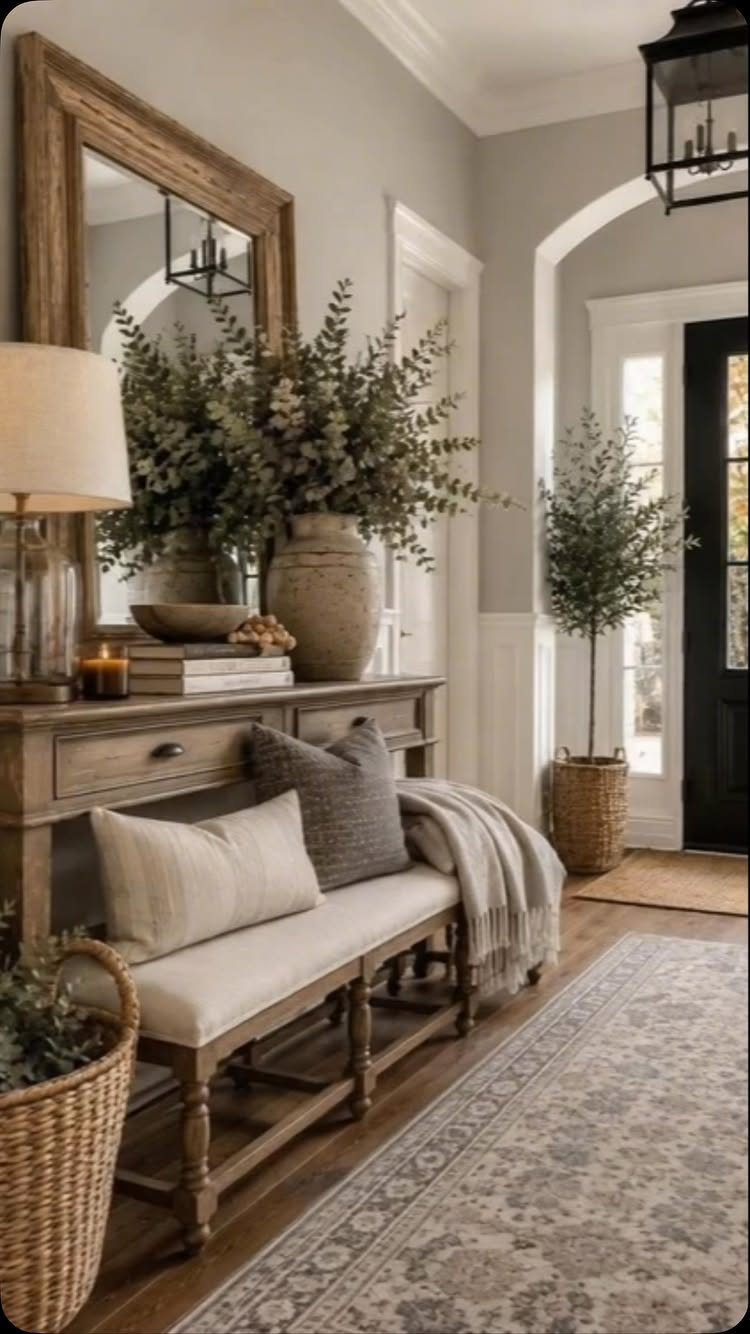 A rustic wooden bench with white cushions sits in a bright farmhouse entryway near a console table.