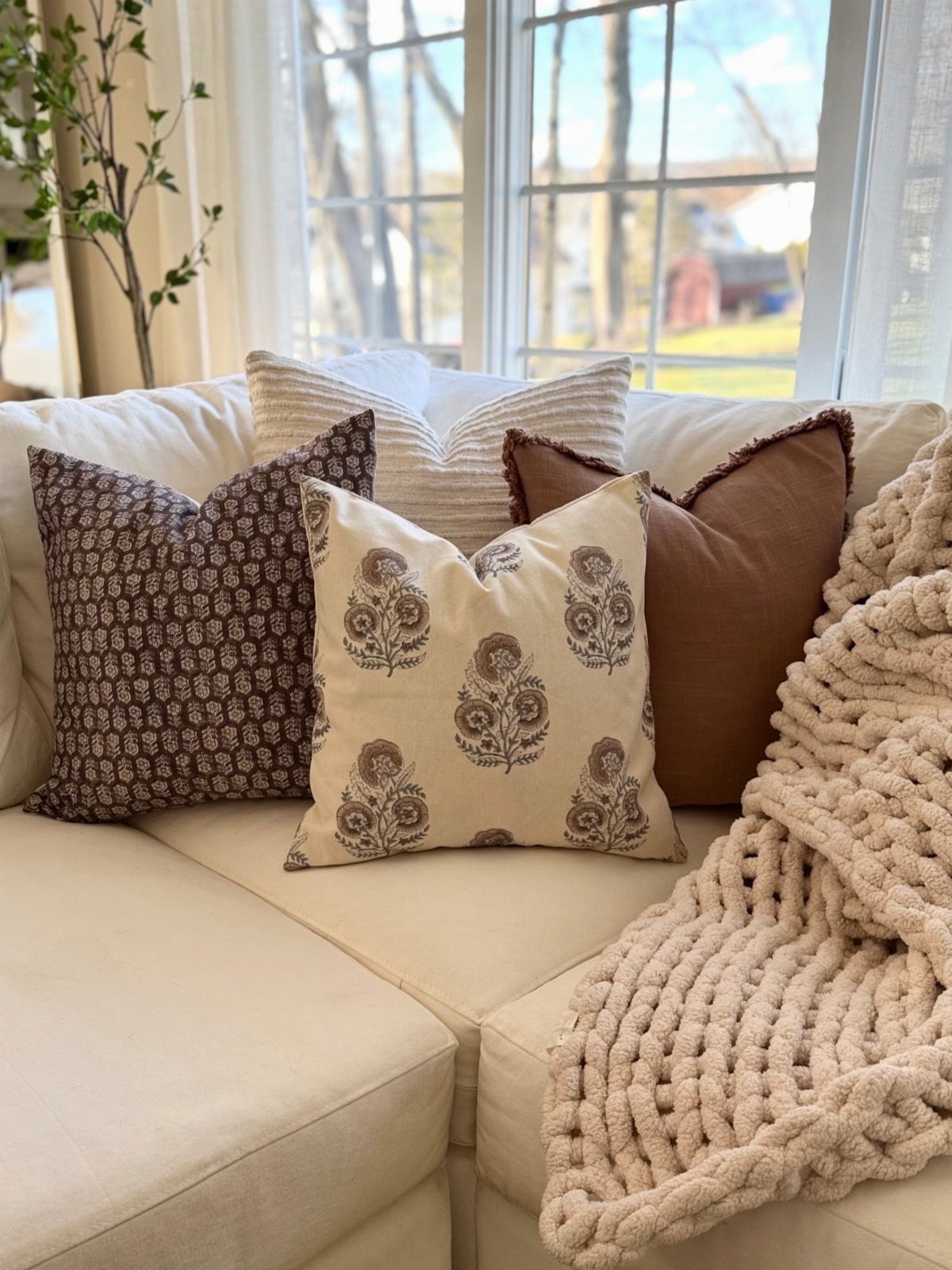 Decorative patterned pillows and a chunky knit throw blanket resting on a white sofa.