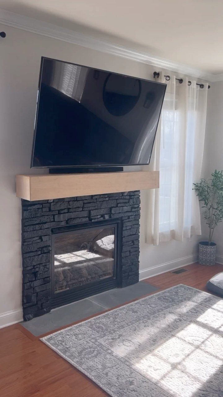 Dark grey stacked stone fireplace with a light wood mantel and a television mounted above.