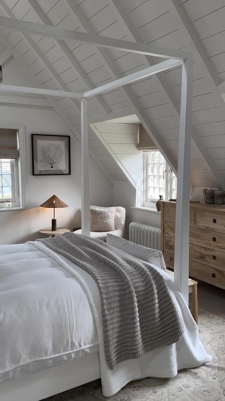 White canopy bed with grey throw blanket in a bright attic bedroom with shiplap walls.