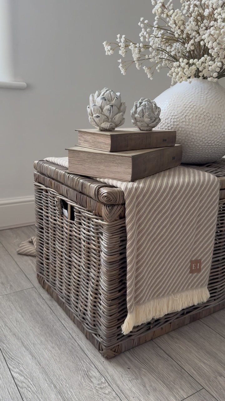 A grey wicker storage trunk decorated with wooden blocks, artichoke sculptures, and a cream throw blanket.