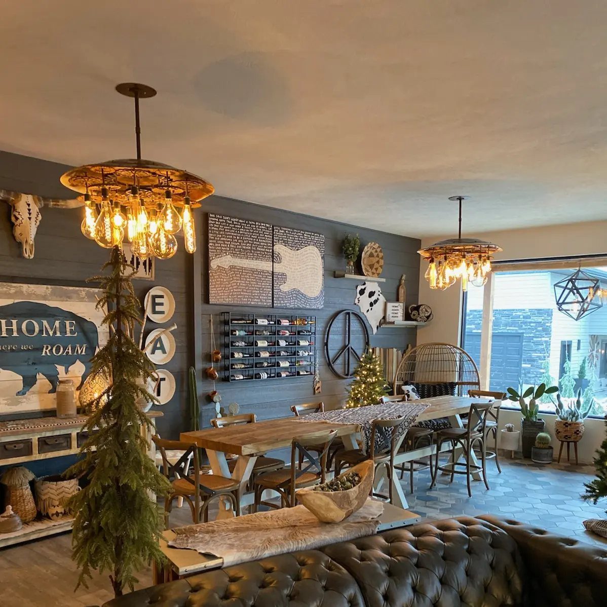 Two ornate wrought-iron chandeliers hanging above a rustic dining room with grey shiplap walls.