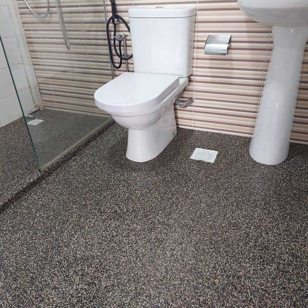 Dark grey epoxy flake flooring in a bathroom with a white toilet and sink.
