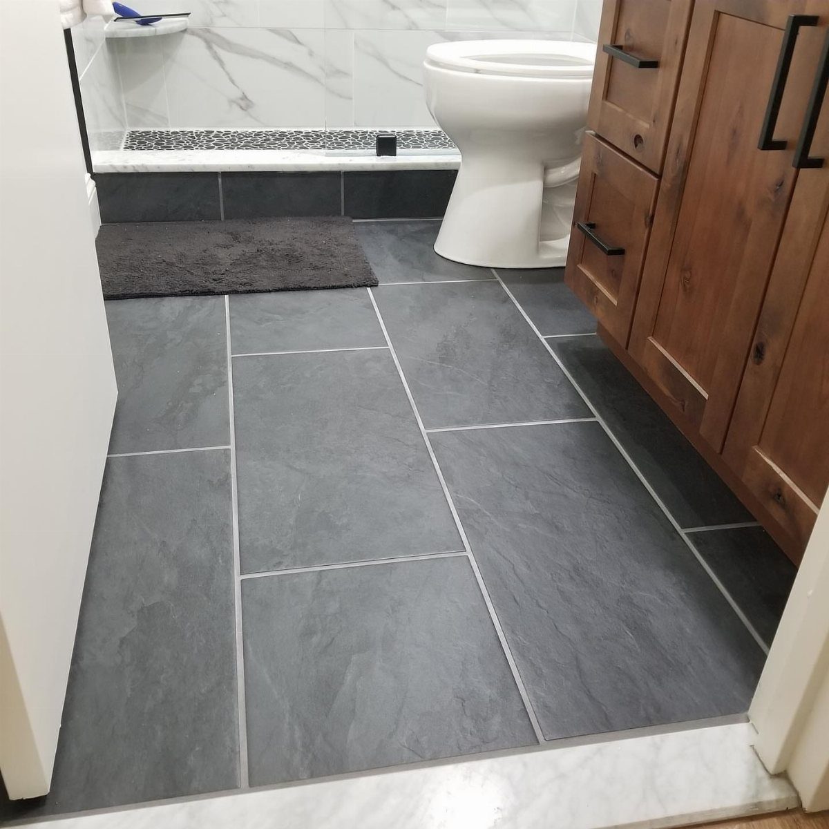 Dark grey large format tiles covering a bathroom floor next to a white toilet.