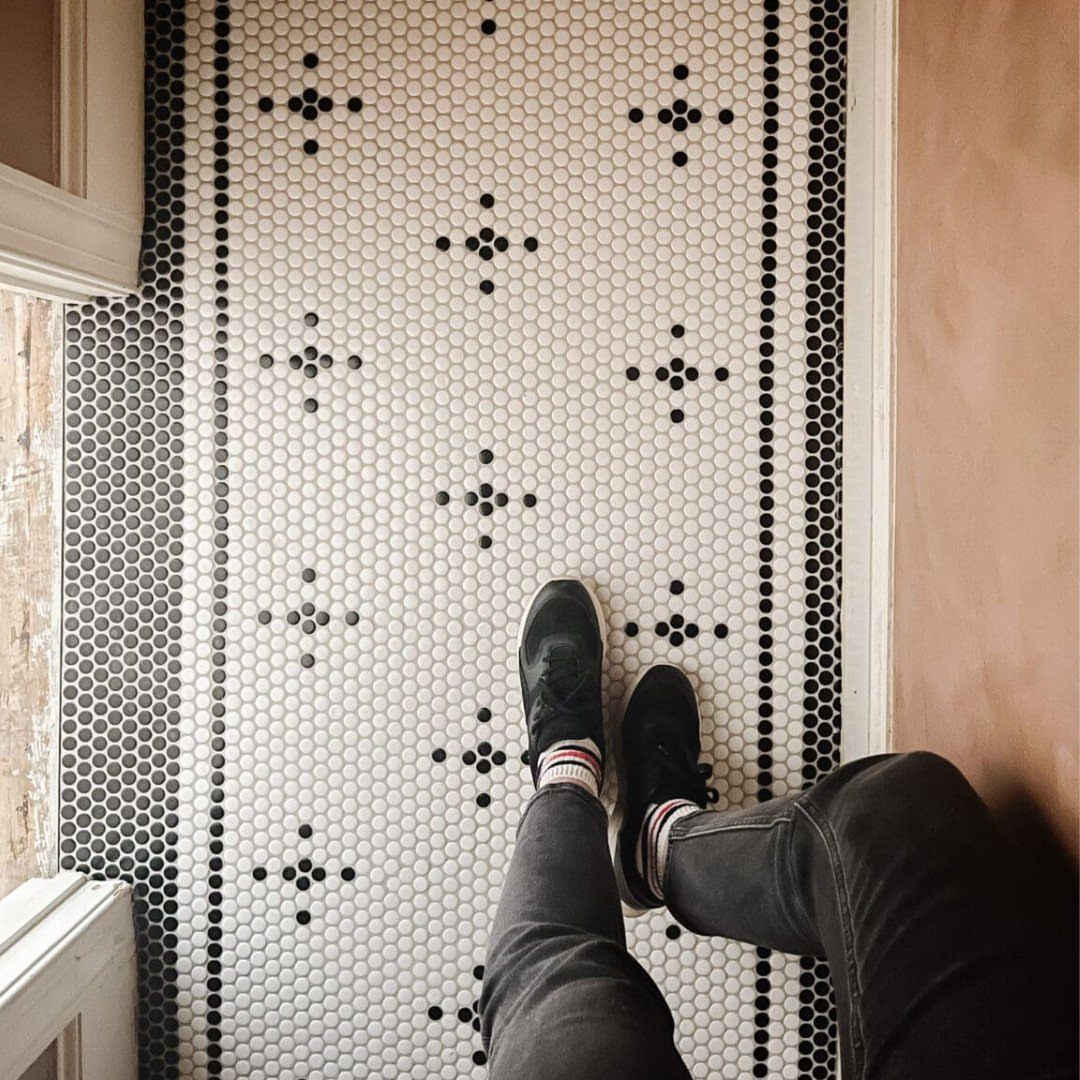 Person standing on white penny tile flooring with black geometric patterns and borders.