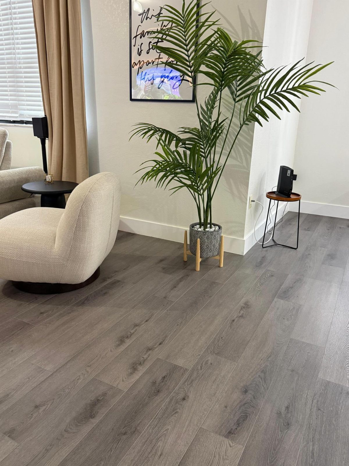 Grey wood-plank flooring in a living room with a white armchair and a large palm plant.
