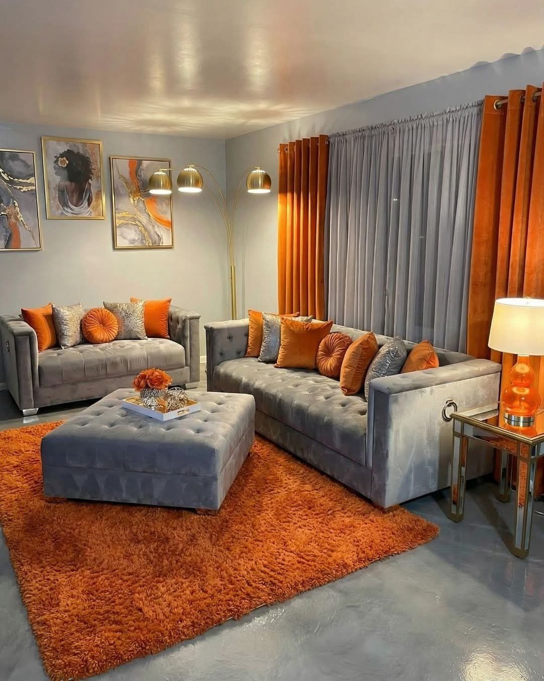 Grey sofas and ottoman accented with orange cushions, an orange rug, and orange curtains in a living room.