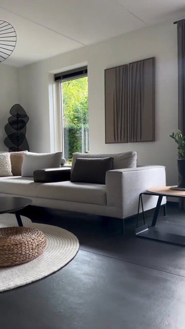 A modern living room with a grey sofa, large textured wall art, and dark grey flooring.