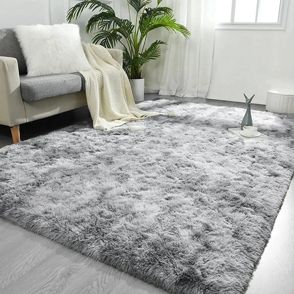 Grey shaggy rug on a light grey floor next to a sofa and potted plant.