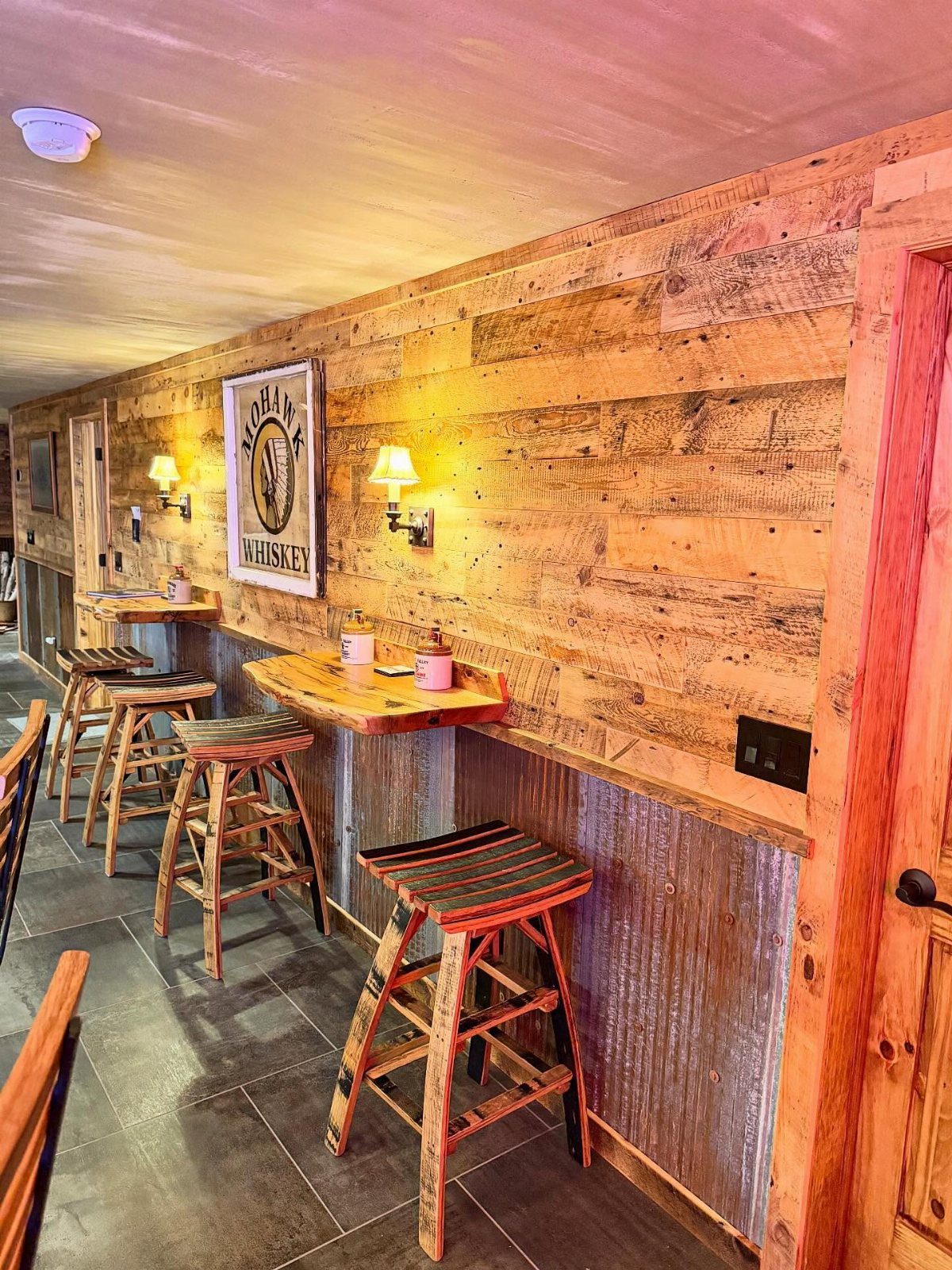 Rustic bar with wood plank upper walls and corrugated metal lower paneling with wooden stools.