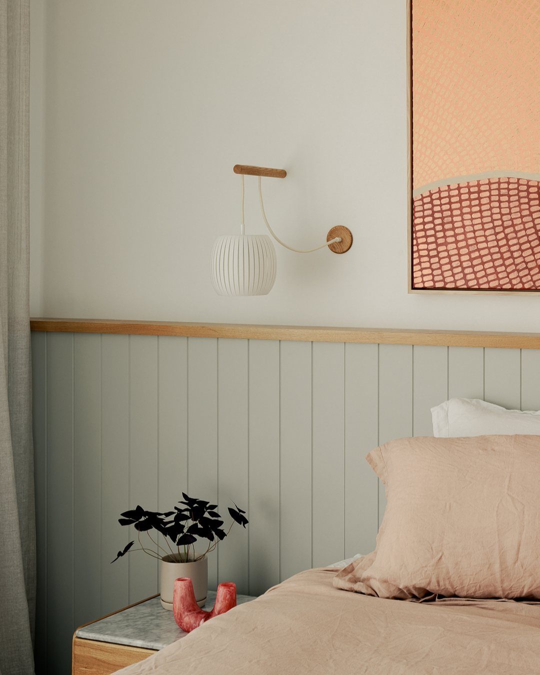 Vertical grey slat paneling with a wooden top rail behind a bed with peach linens.