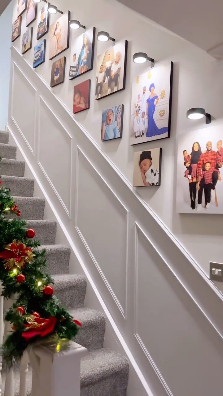 White wainscoting paneling on a staircase wall decorated with framed family photos and small lights.