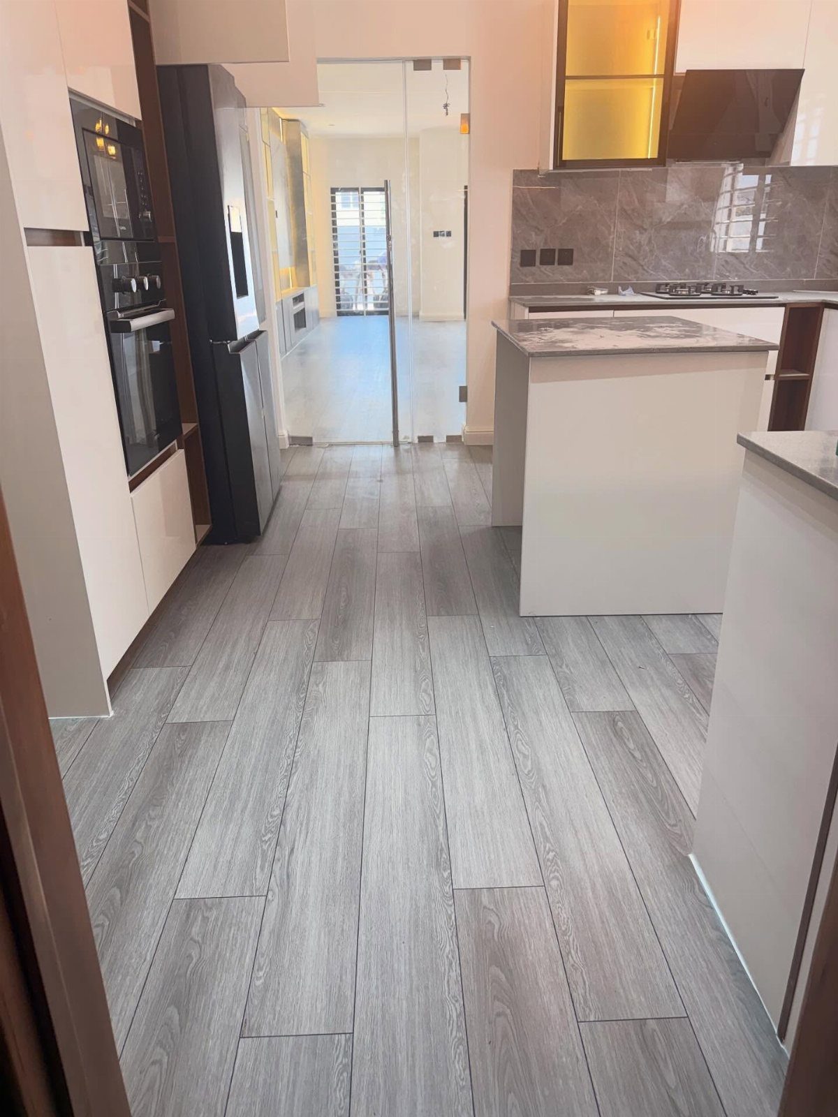 Kitchen Flooring for White Cabinets: 11 Ideas That Actually Work 7 Grey wood-textured flooring in a modern kitchen with white cabinets and a central island.