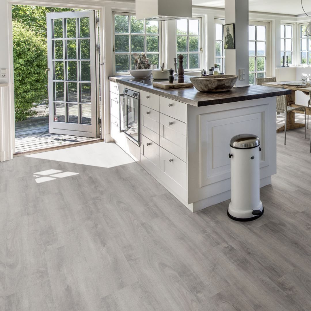 Kitchen Flooring for White Cabinets: 11 Ideas That Actually Work 5 Gray wood-look flooring in a bright kitchen with white cabinets and an open glass door.