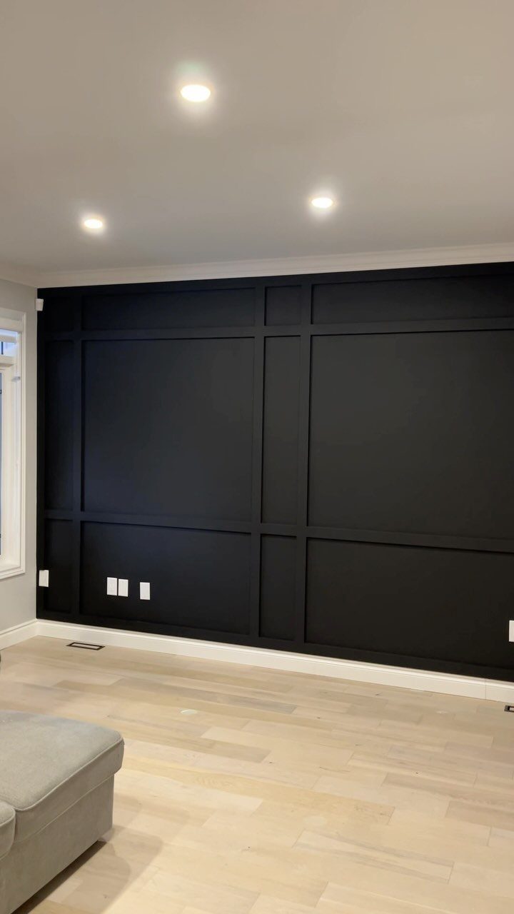 A black accent wall with decorative picture frame molding in a bright living room.
