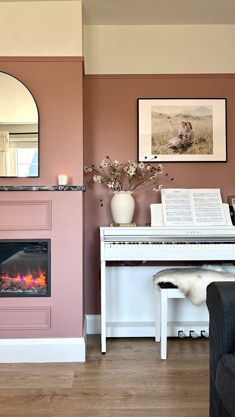 A muted blush pink accent wall in a living room with a white piano and fireplace.