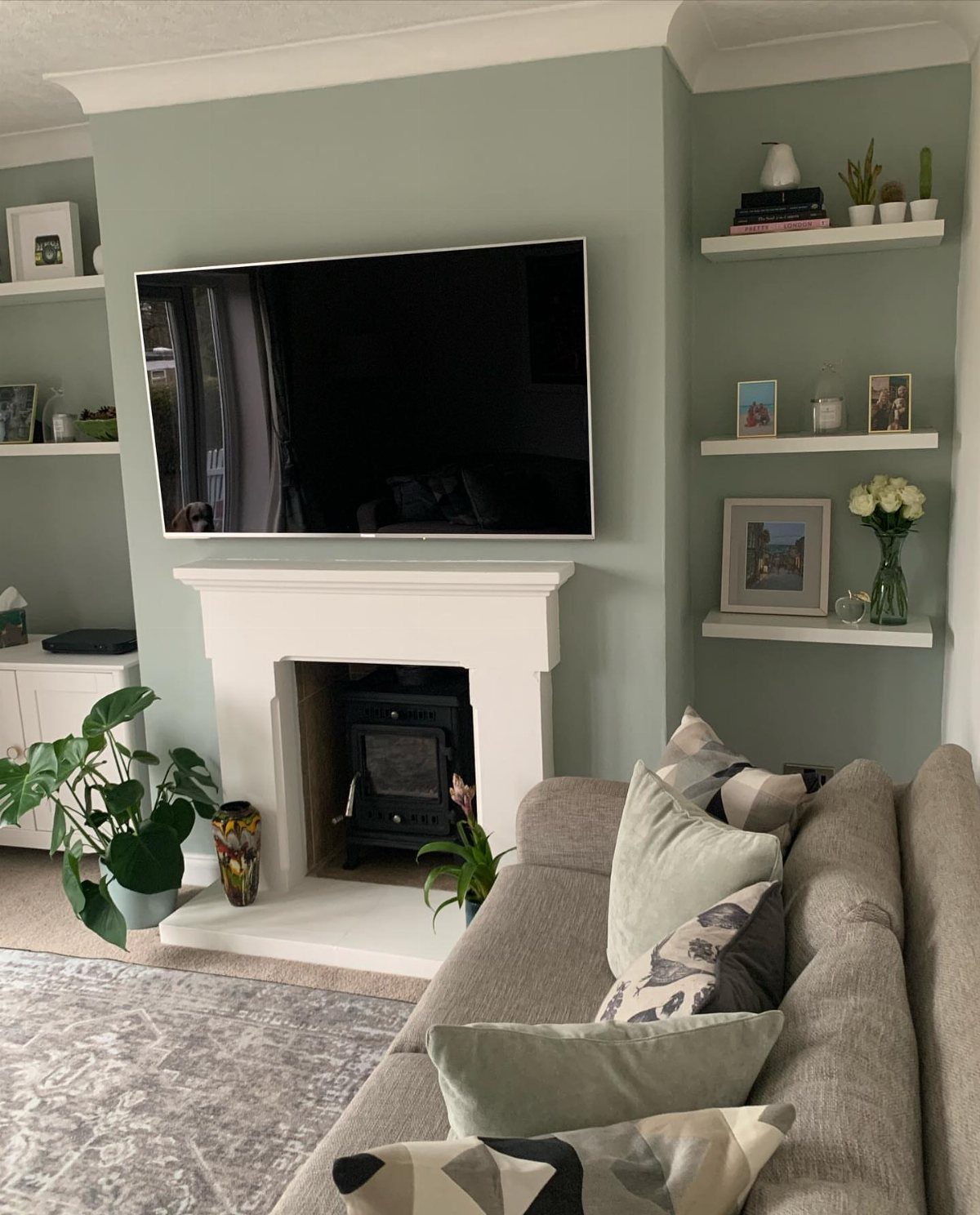 Soft sage green accent wall in a living room with a white fireplace and grey sofa.