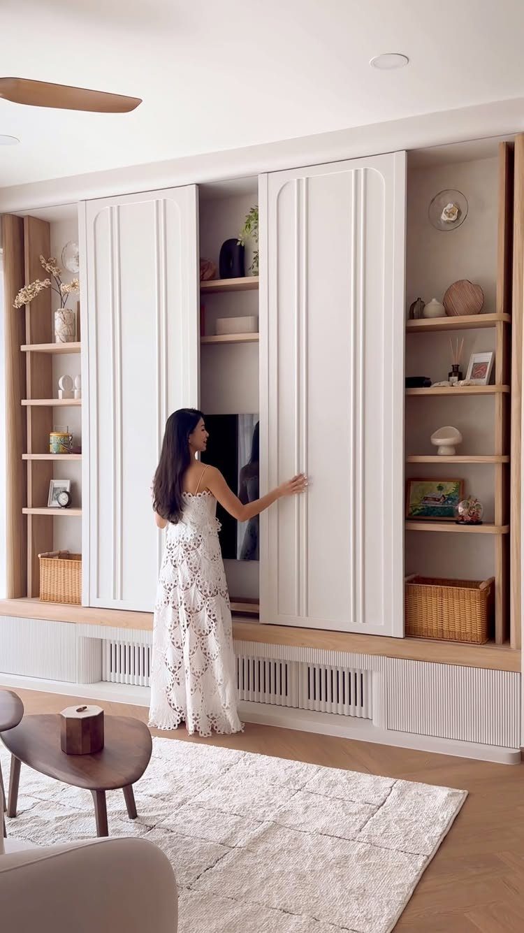 A woman reaches for large white sliding doors on a built-in wall unit with wooden shelves.