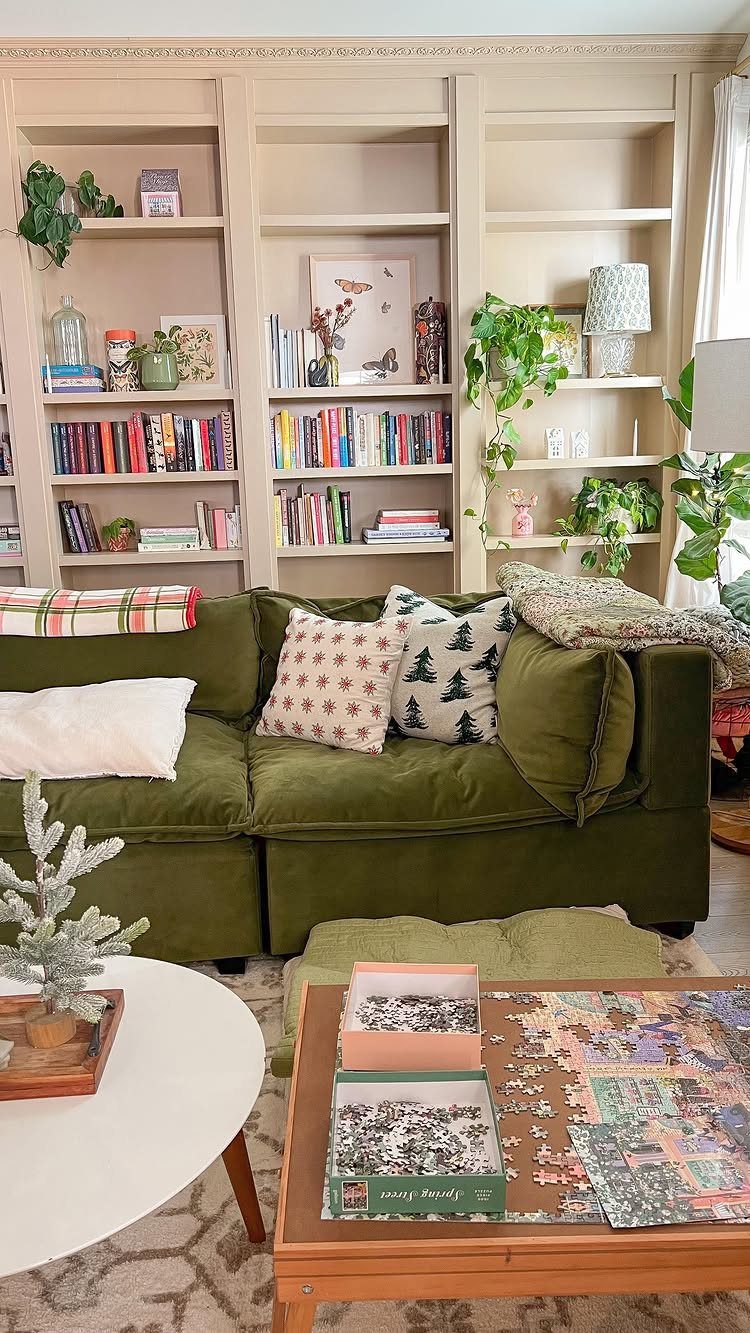 Beige built-in bookshelves filled with books and plants behind a green velvet sofa.