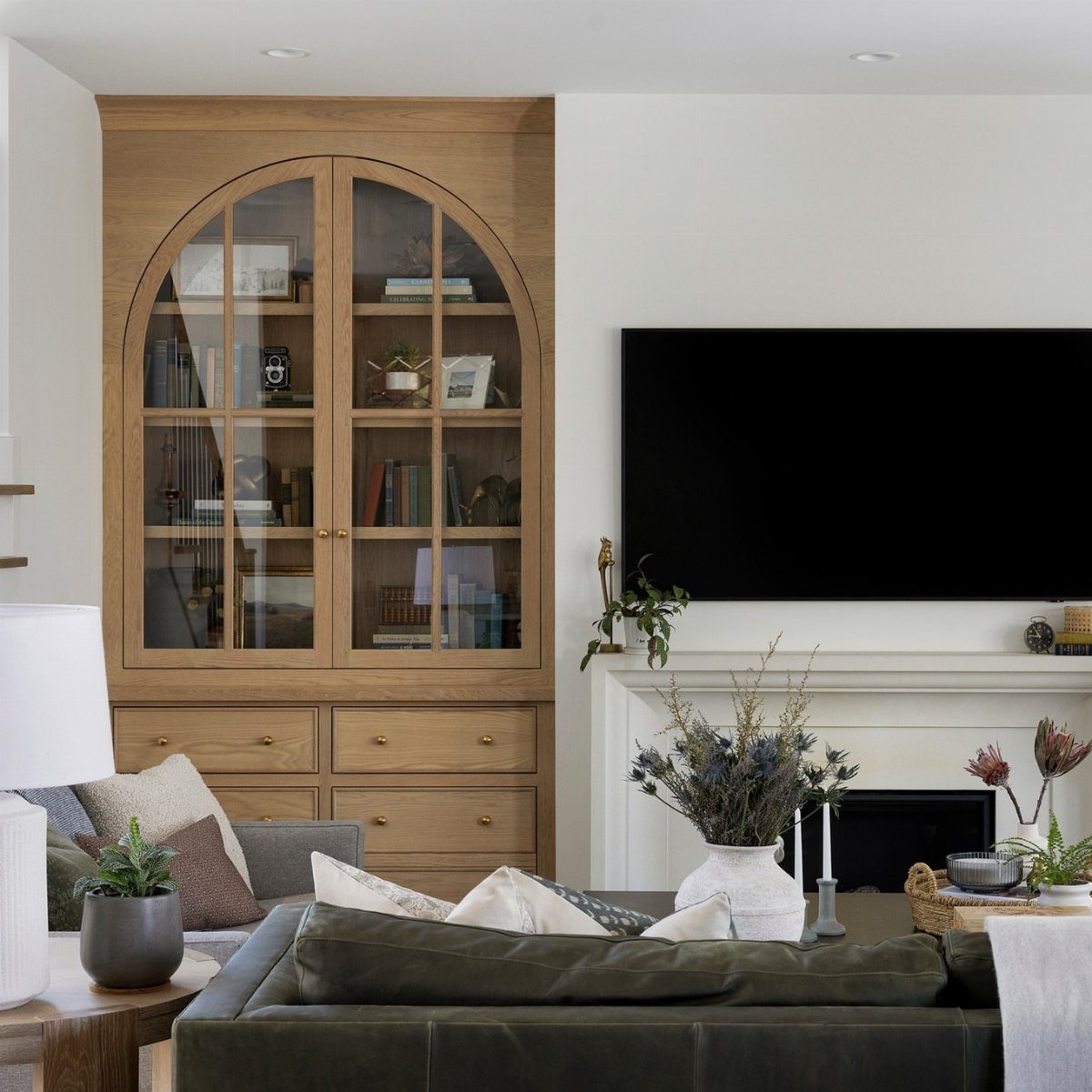 Light wood built-in unit with arched glass doors and bottom drawers in a living room.