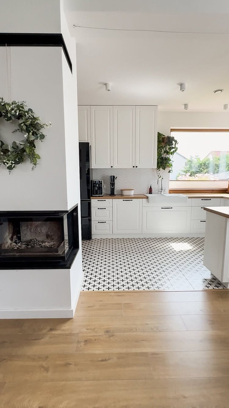 Light wood flooring transitioning into black and white patterned tiles in a bright kitchen.
