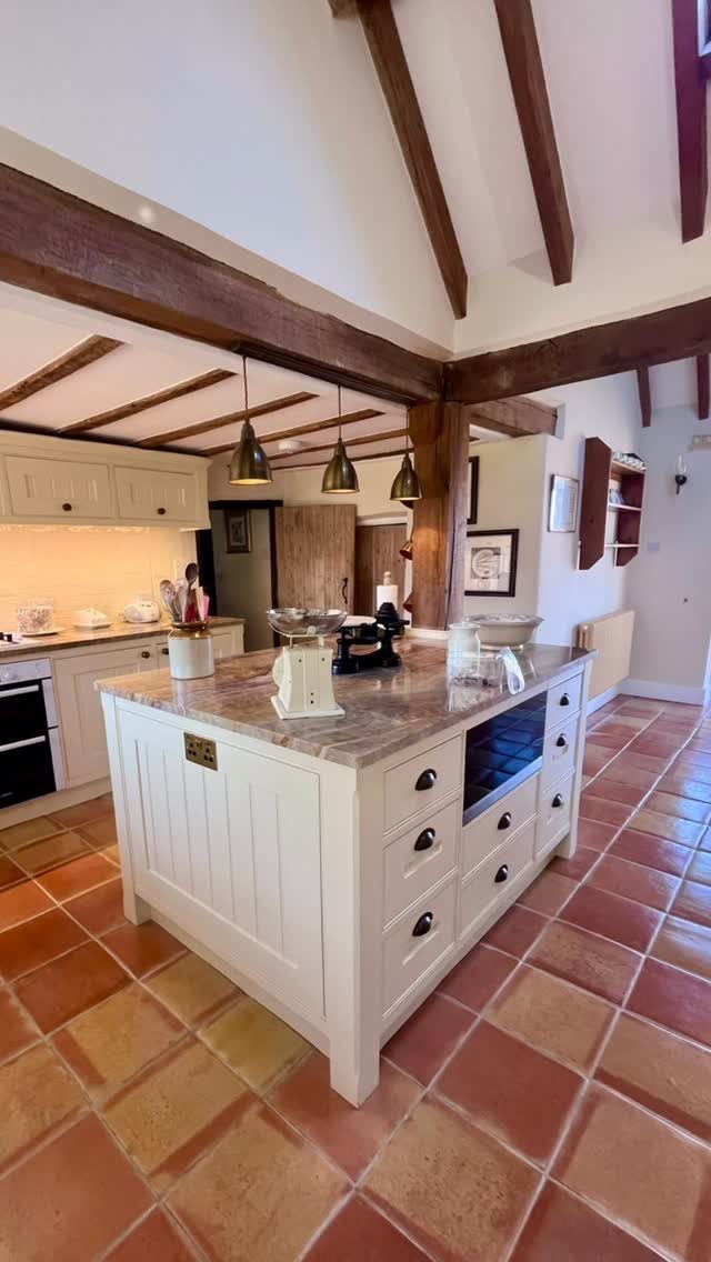 Terracotta tiles cover the floor of a rustic kitchen with white cabinetry and wooden ceiling beams.