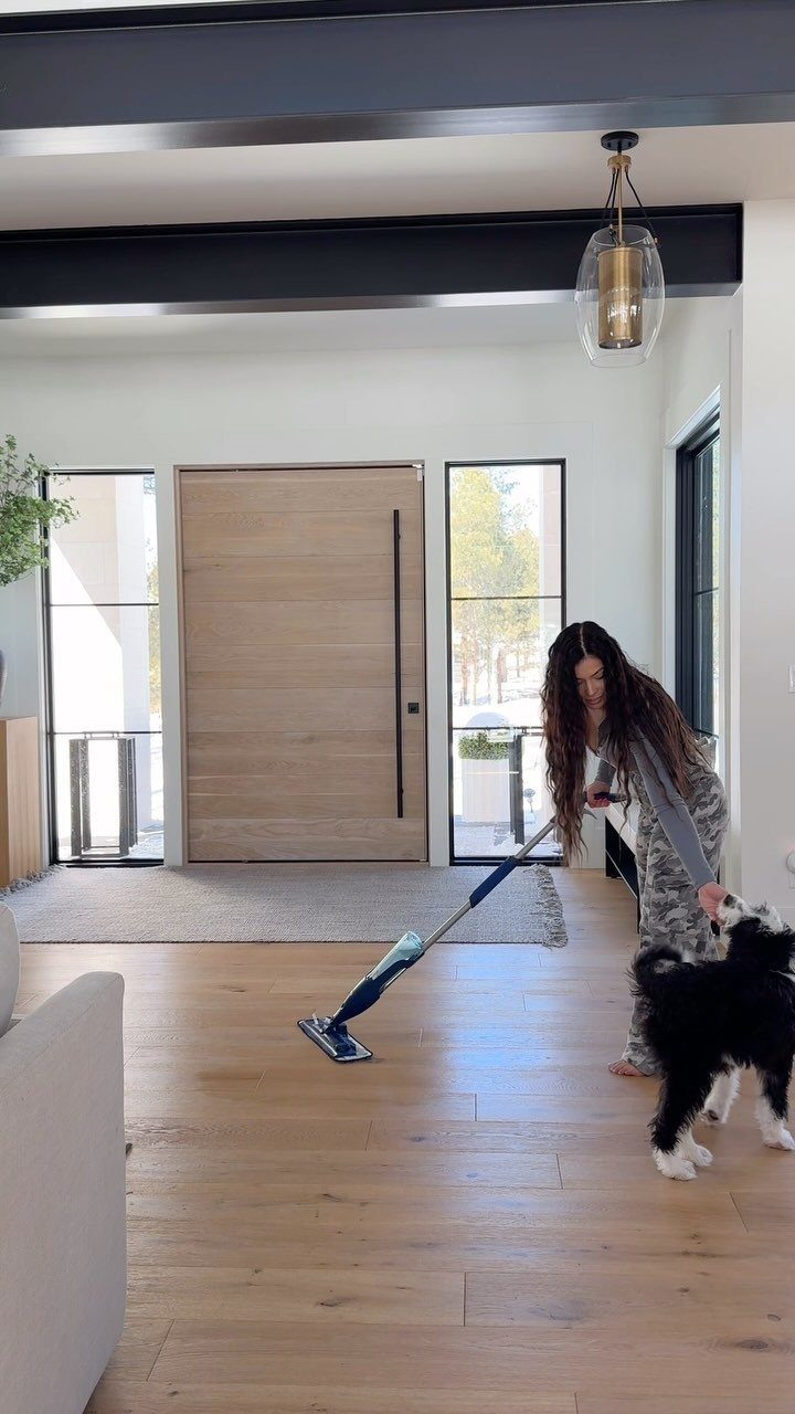 A woman mopping light wood-colored vinyl flooring in a bright, modern farmhouse style room.