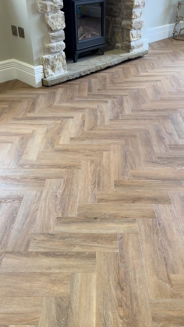 Herringbone pattern wood-effect vinyl flooring in a room with a stone fireplace.