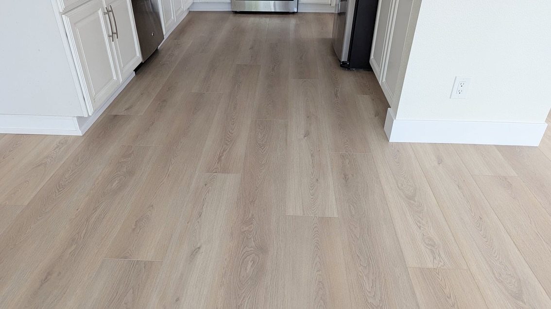 Light wood-look vinyl flooring planks installed in a bright kitchen with white cabinetry.