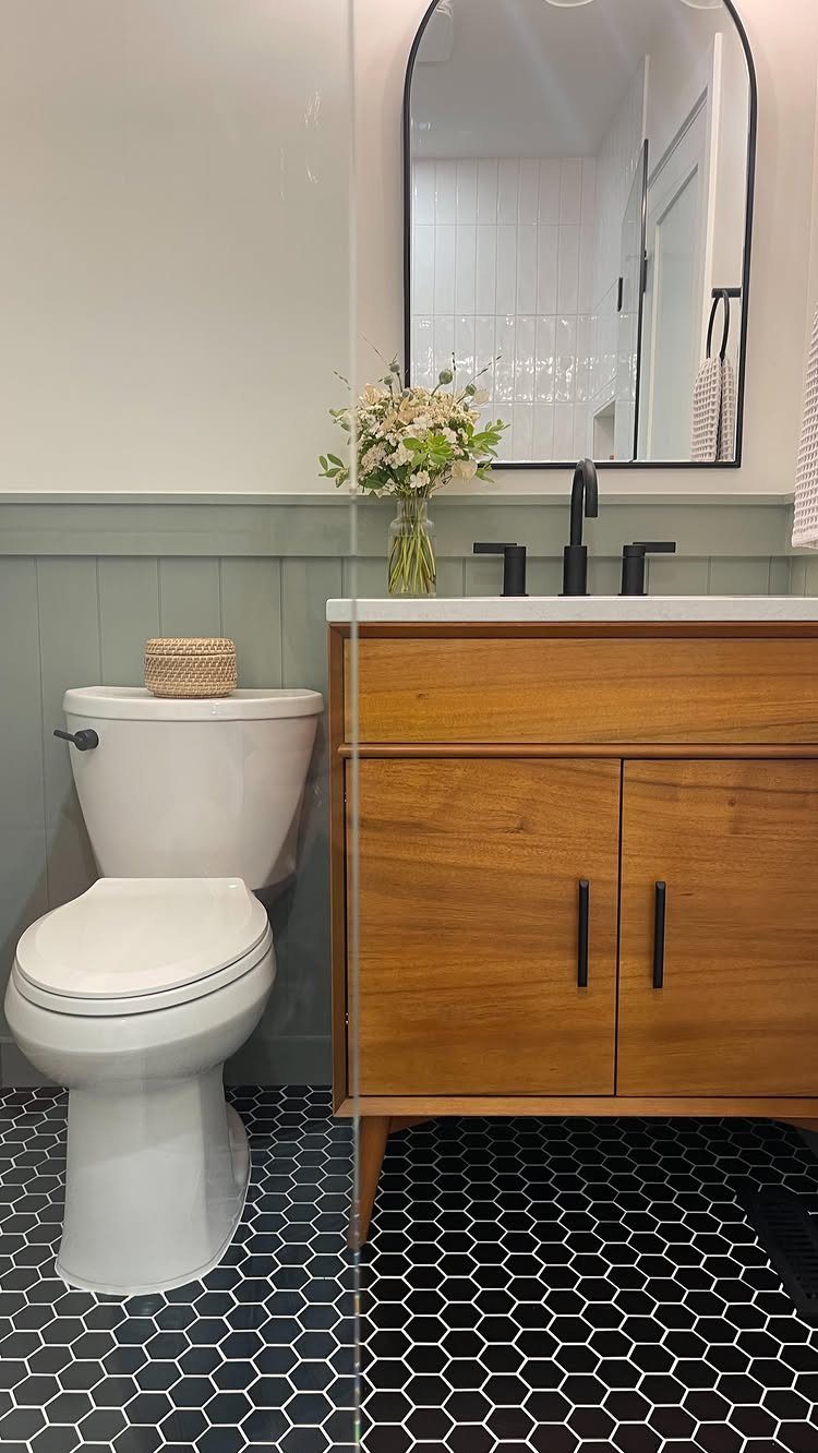 Sage green board and batten wainscoting in a bathroom with a wooden vanity and hexagonal tiles.