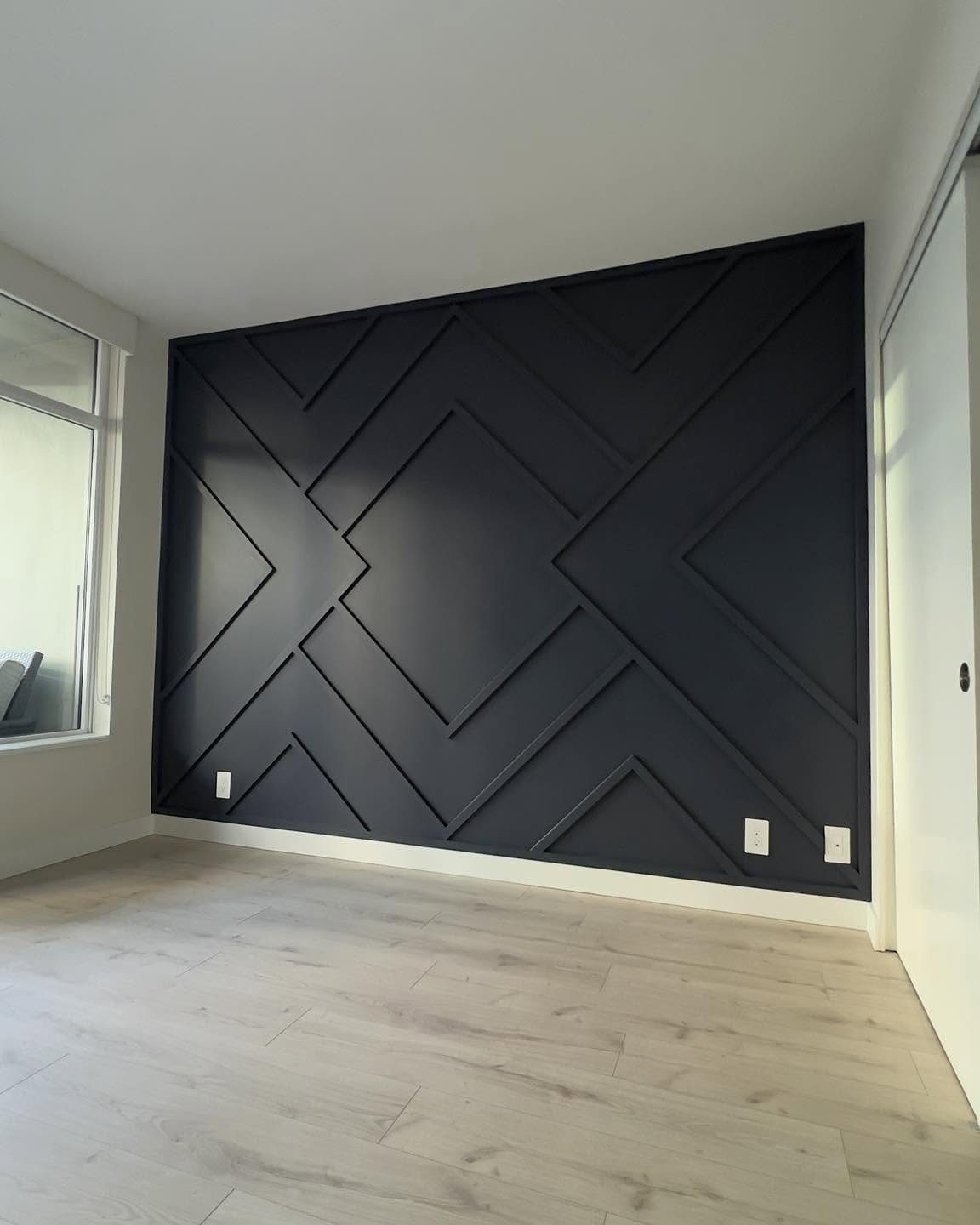 Dark charcoal geometric wainscoting with raised angular patterns on an accent wall in a room.