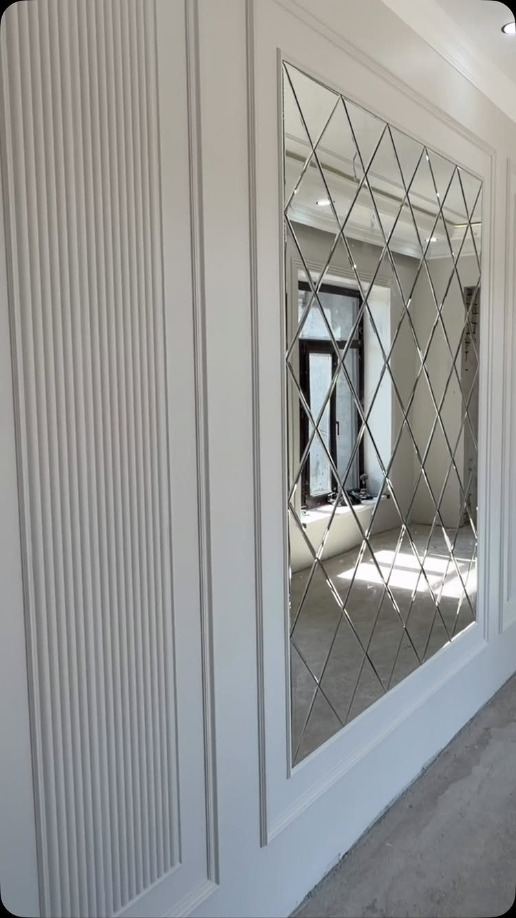 White paneled walls with a large diamond-patterned mirror reflecting a bright room.