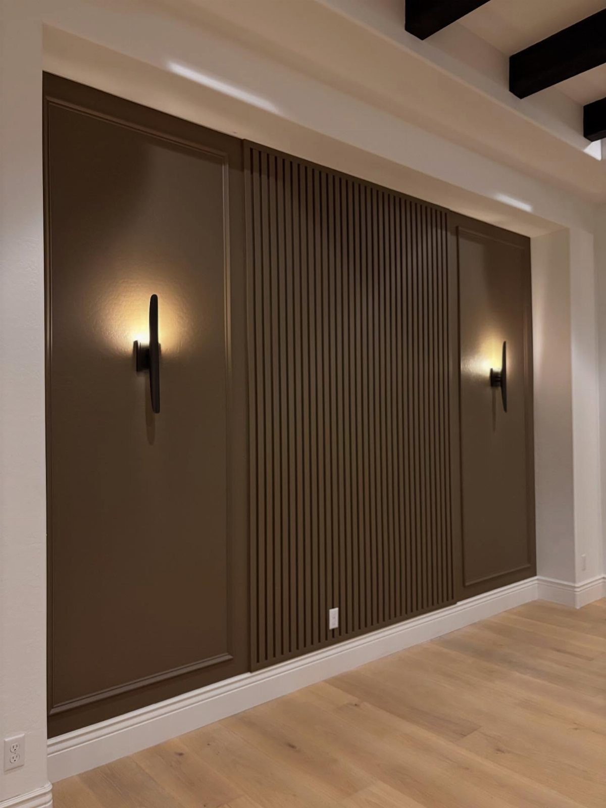 Brown wainscoting with flat panels and vertical wood slats on a wall with sconces.
