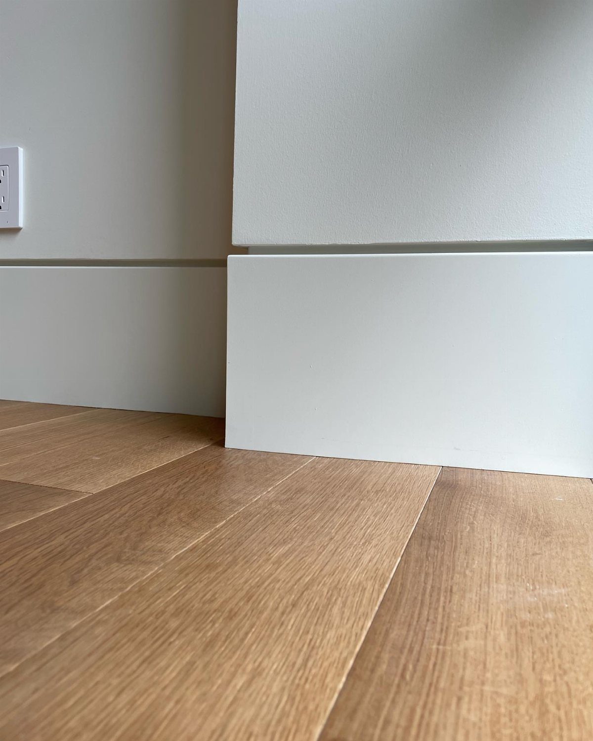 Wall Moulding Design: 11 Styles That Work in Every Room 3 White baseboard moulding meeting a white wall and light wood plank flooring in a corner.