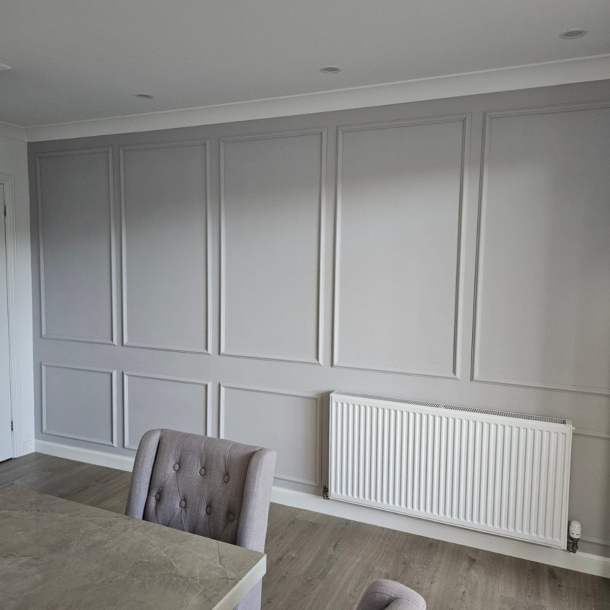 Wall Moulding Design: 11 Styles That Work in Every Room 5 Grey wall decorated with large rectangular picture frame moulding panels and a white radiator below.