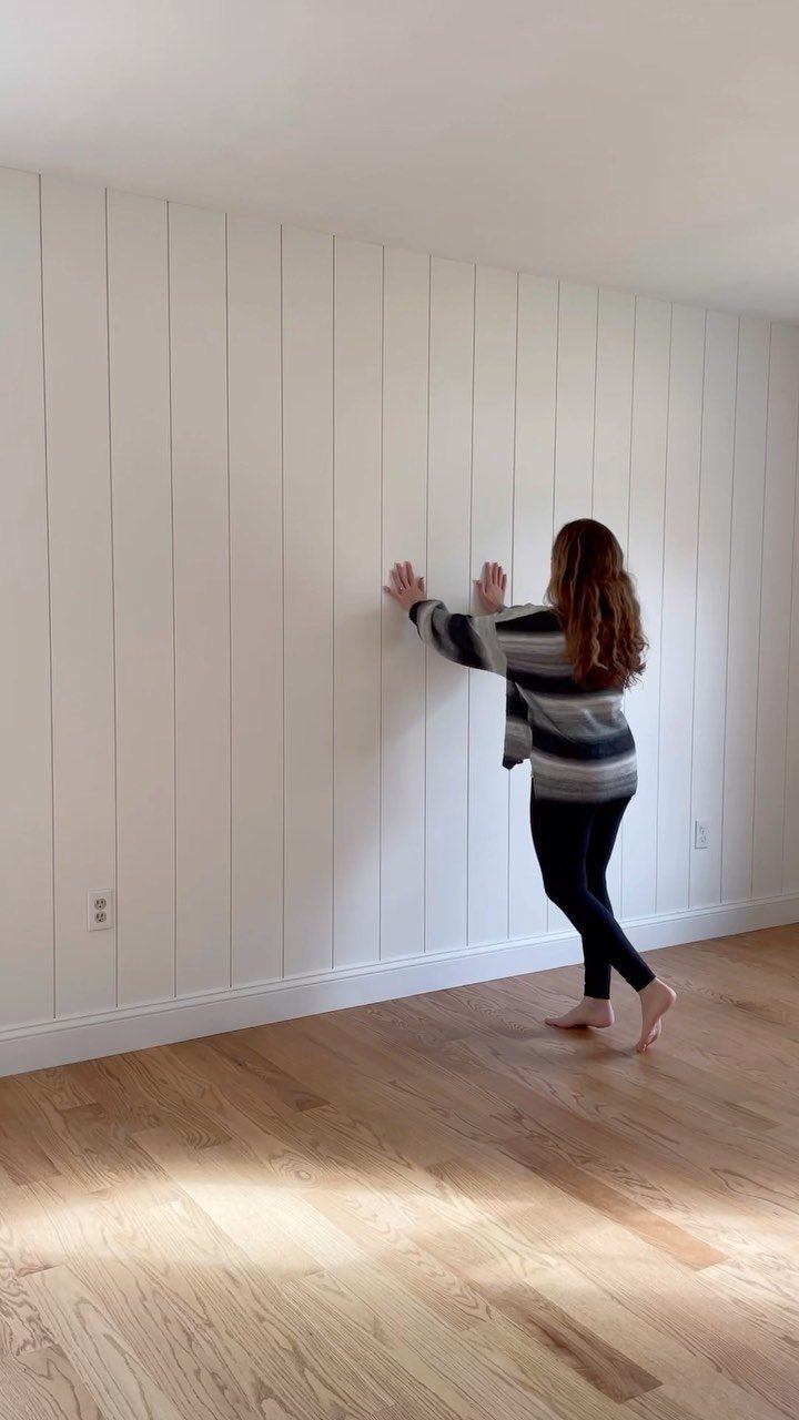 Wall Moulding Design: 11 Styles That Work in Every Room 2 A woman touching a white vertical shiplap accent wall in a bright room.