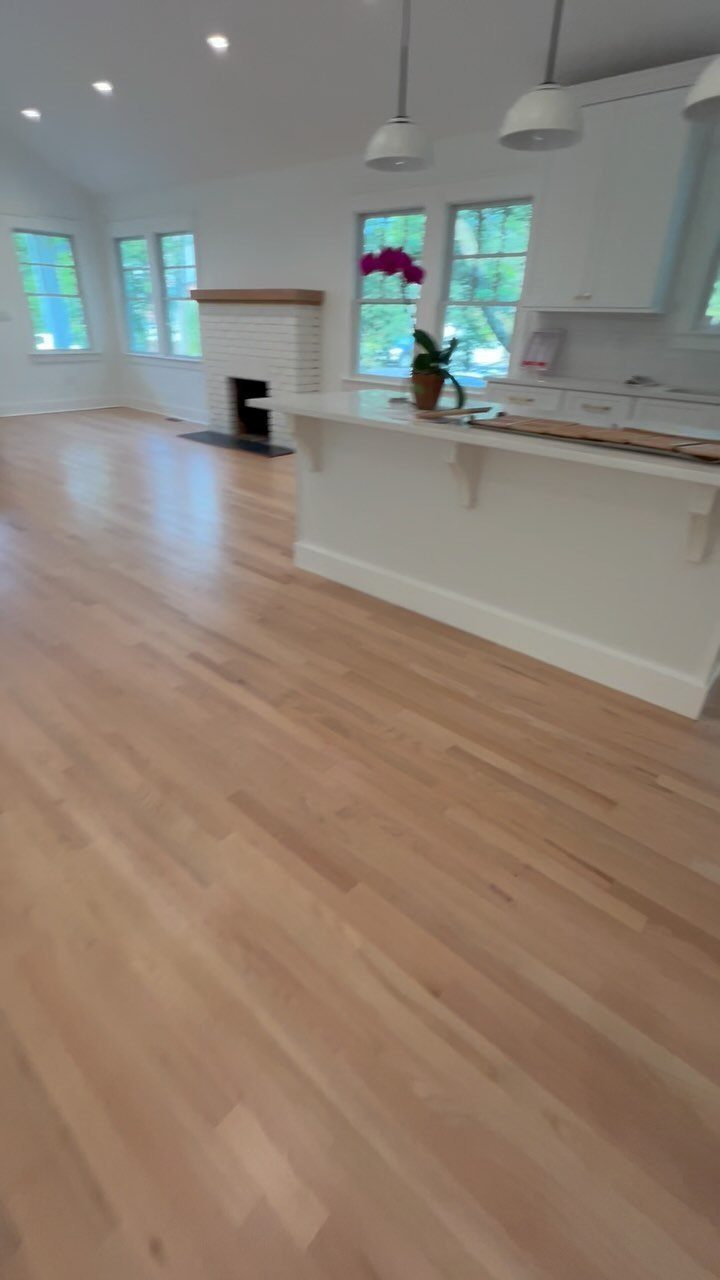 Light-toned hardwood flooring in a bright, modern kitchen with white cabinets and large windows.