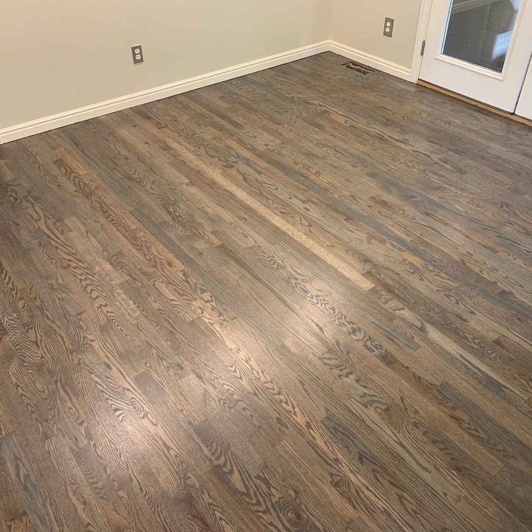 Oak hardwood flooring with a gray driftwood stain installed in a room with white baseboards.